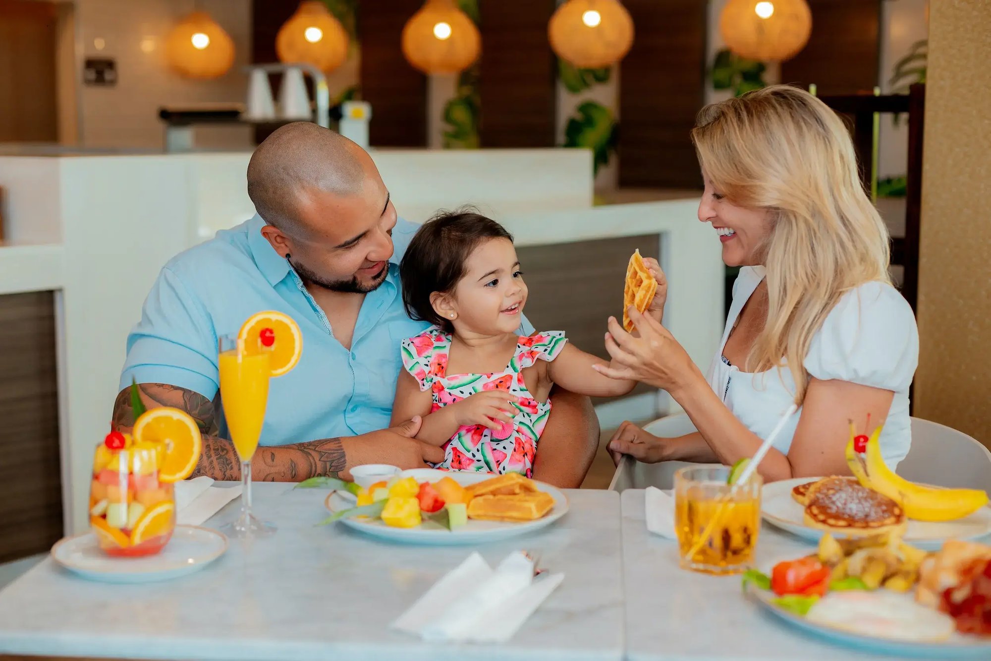happy family sitting eating breakfast smiling with lots of food